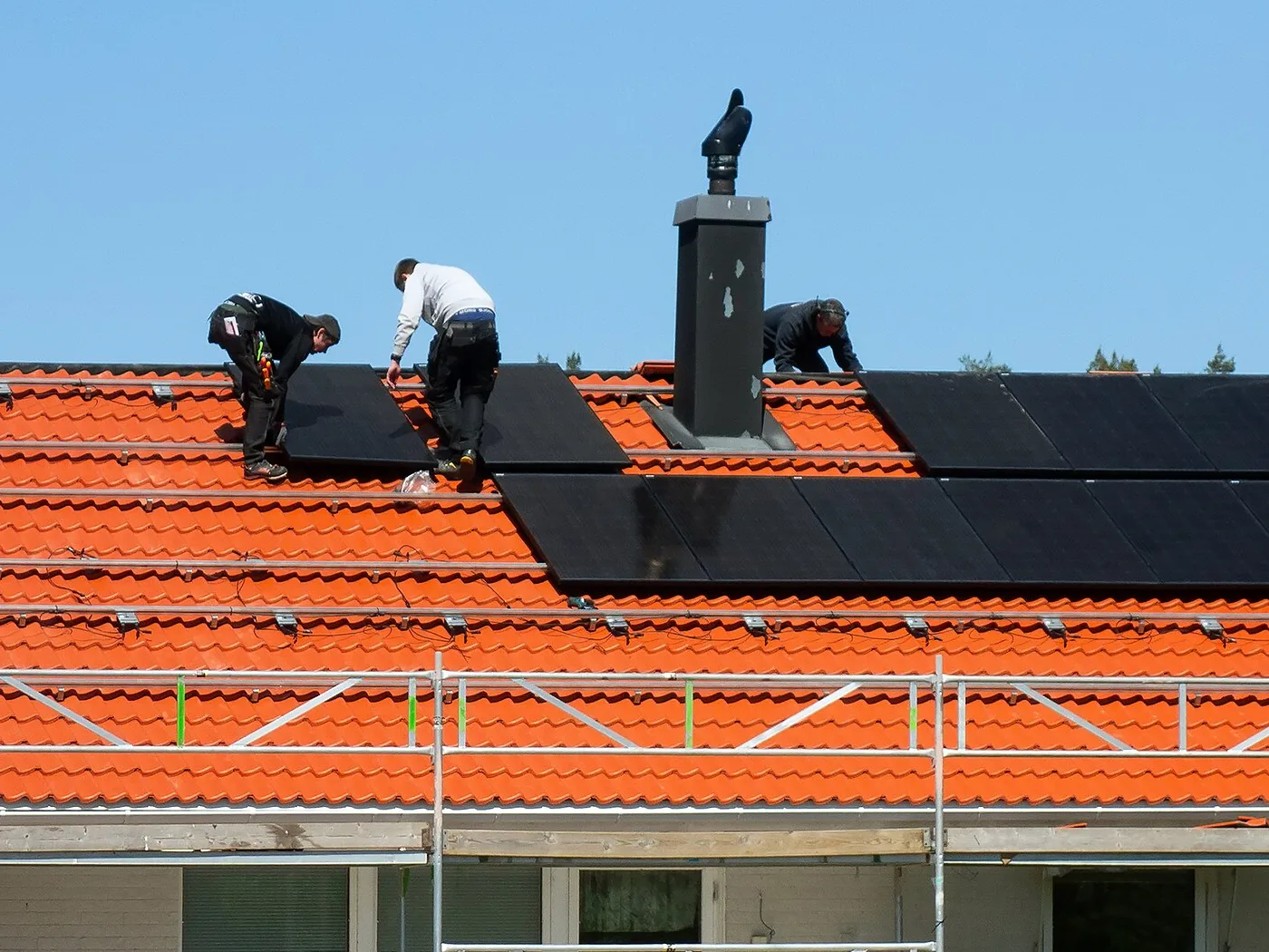 Drei Monteure befestigen Photovoltaikmodule auf einem Hausdach